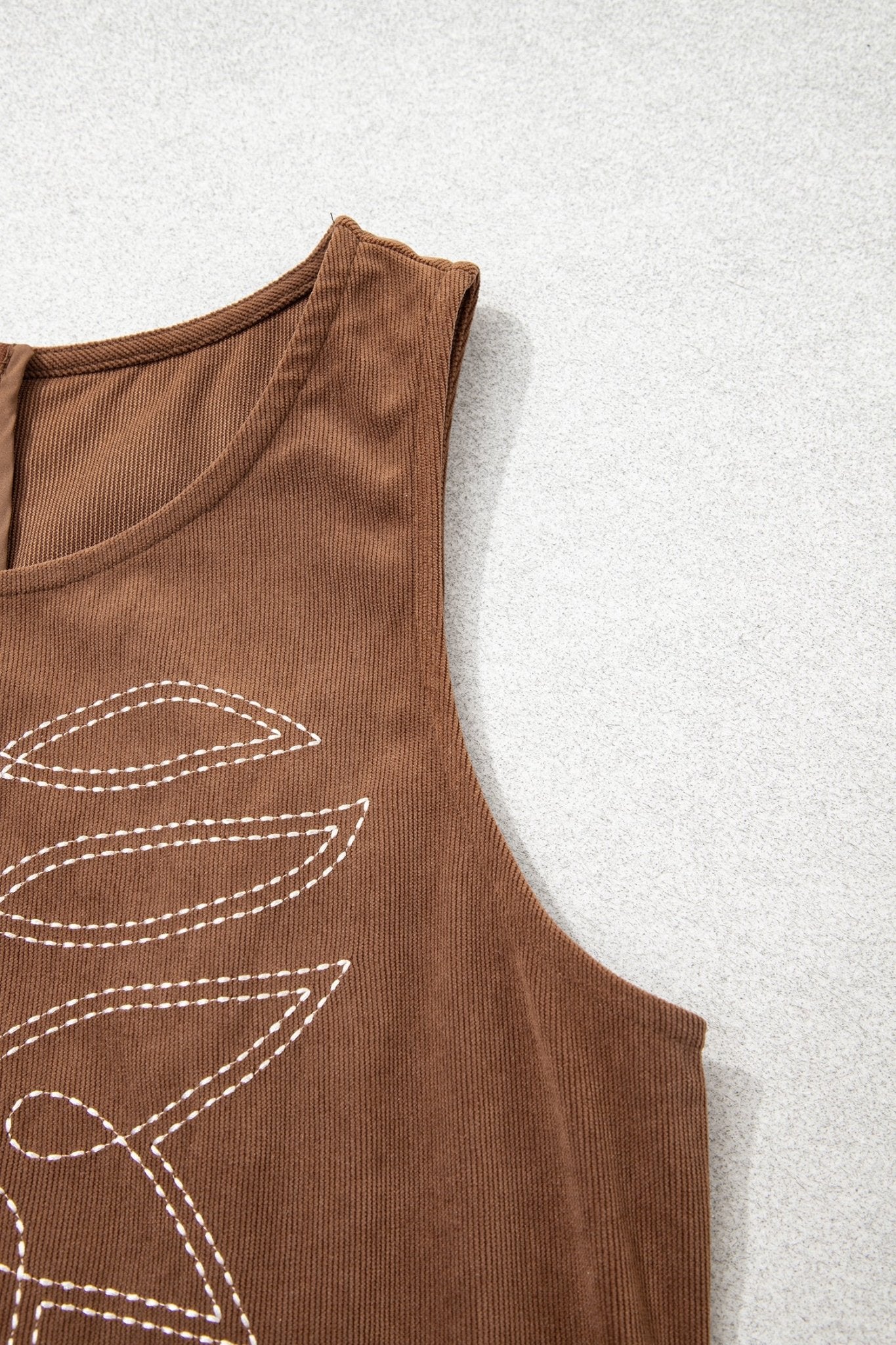 Close-up of brown ribbed sleeveless top with white dashed leaf embroidery.