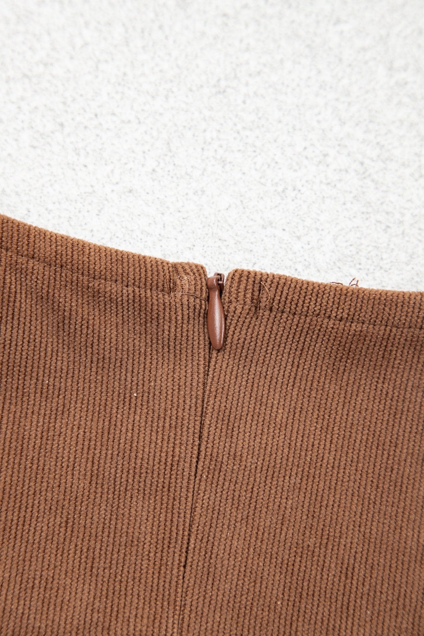 Close-up of brown ribbed knit garment with inner neck opening and zipper pull.