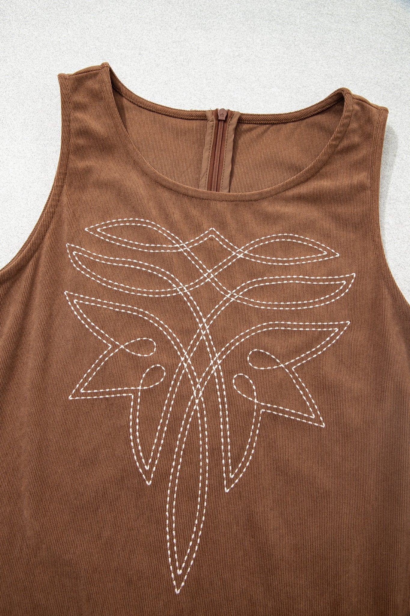 Brown sleeveless top with white abstract leaf-like embroidery on front.