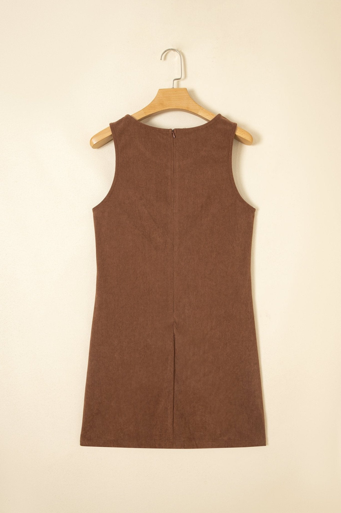 A brown sleeveless dress hanging on a wooden hanger against a plain beige wall.