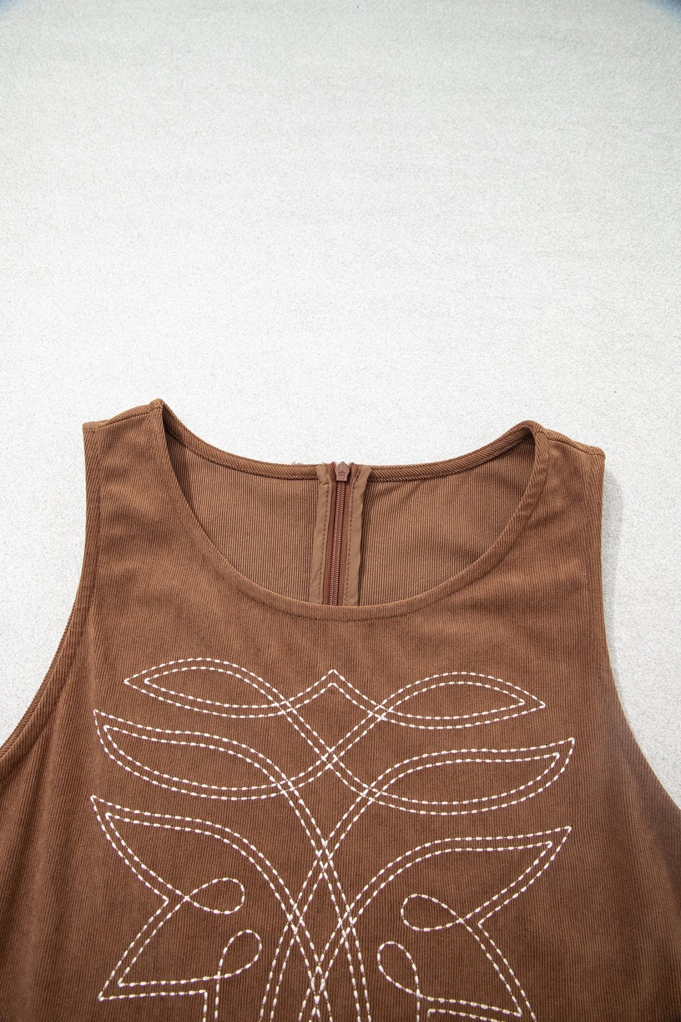 Close-up of brown sleeveless top with zipper and white leaf-like embroidery.