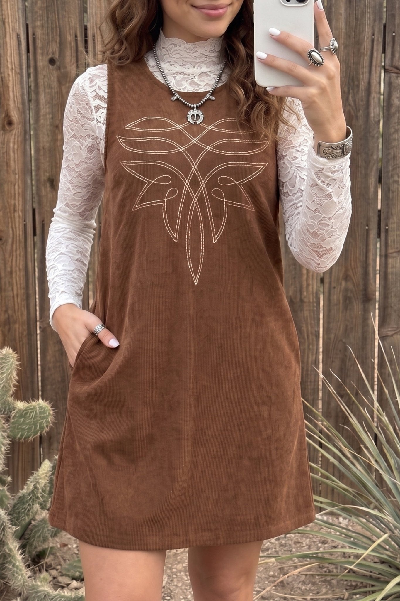 Woman in brown corduroy dress with white butterfly embroidery over a white lace top.