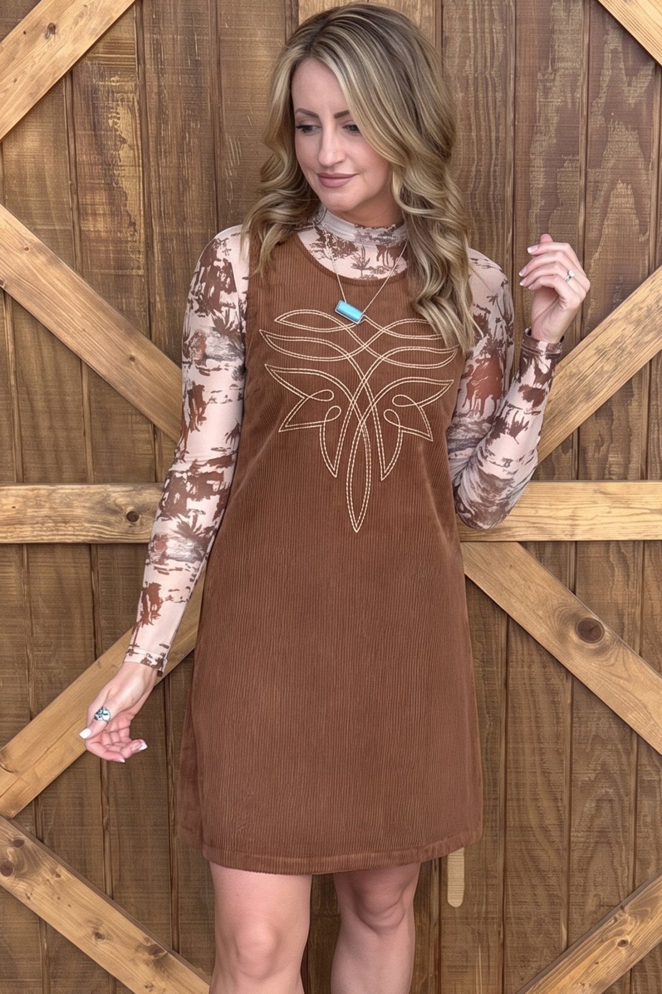 Woman in brown corduroy pinafore over a brown-beige camouflage long-sleeve top.