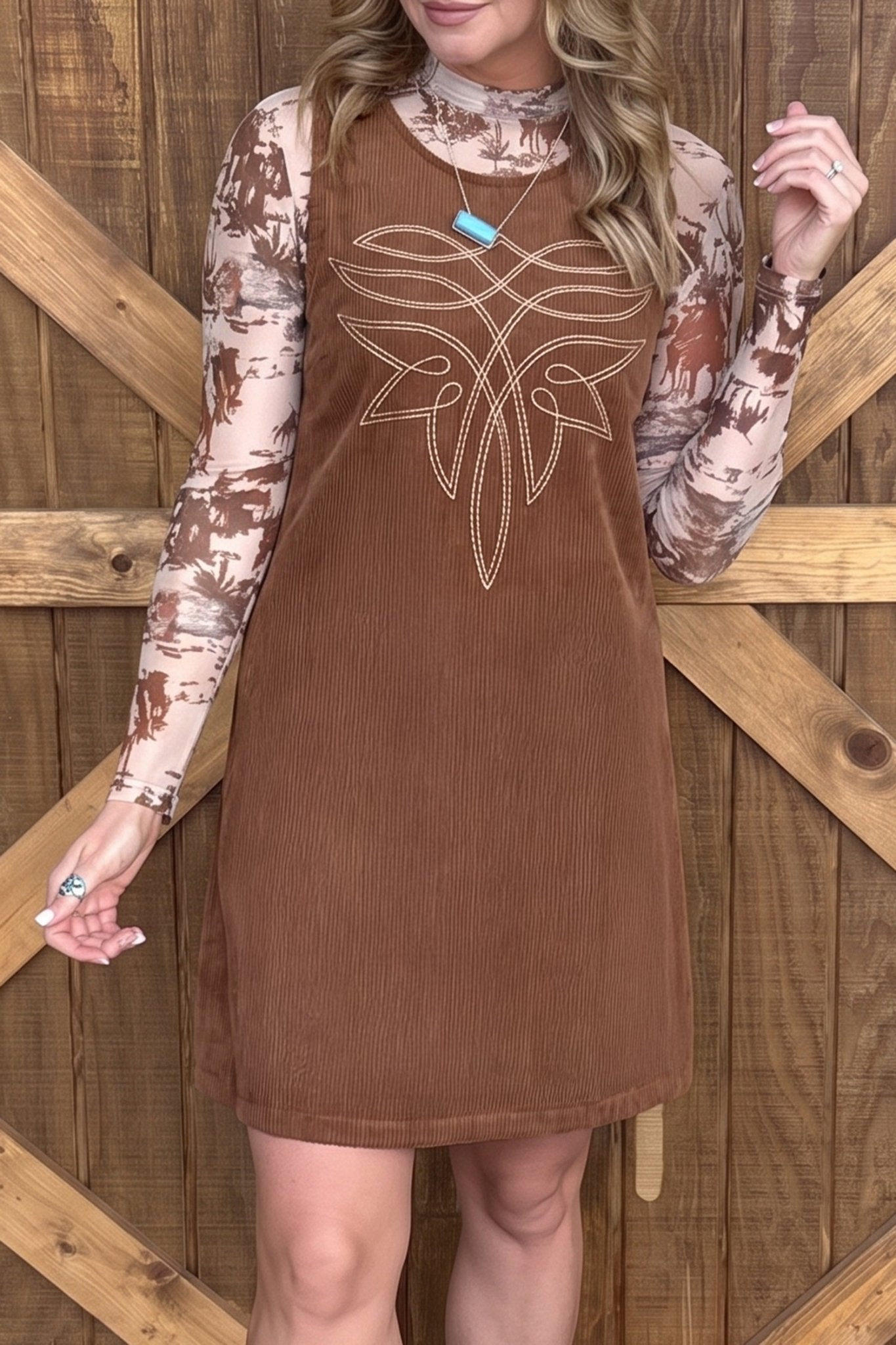 Woman in brown corduroy dress with white chest graphic over a tie-dye long-sleeve top.