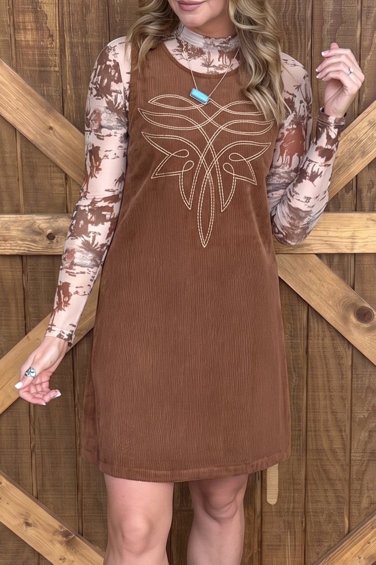 Woman in brown corduroy dress with white chest graphic over a tie-dye long-sleeve top.