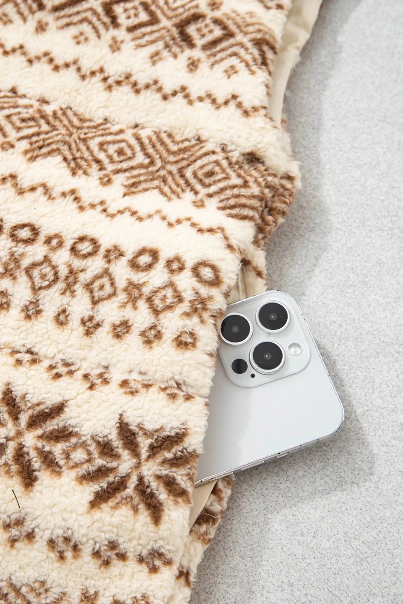 Close-up of cream-brown patterned fleece blanket with white smartphone underneath.