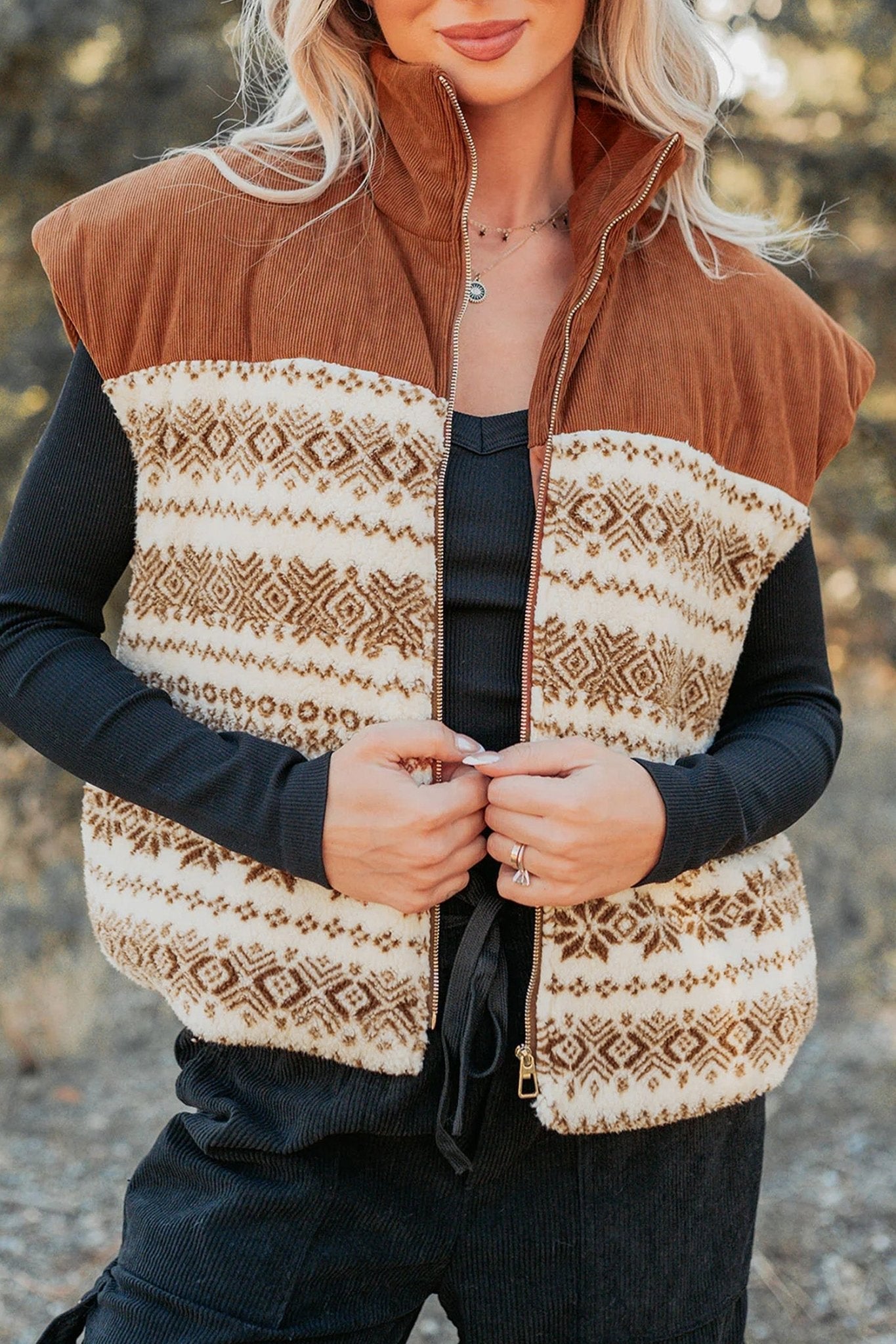 Woman in brown-cream patterned zip-up vest over black long-sleeve top outdoors.