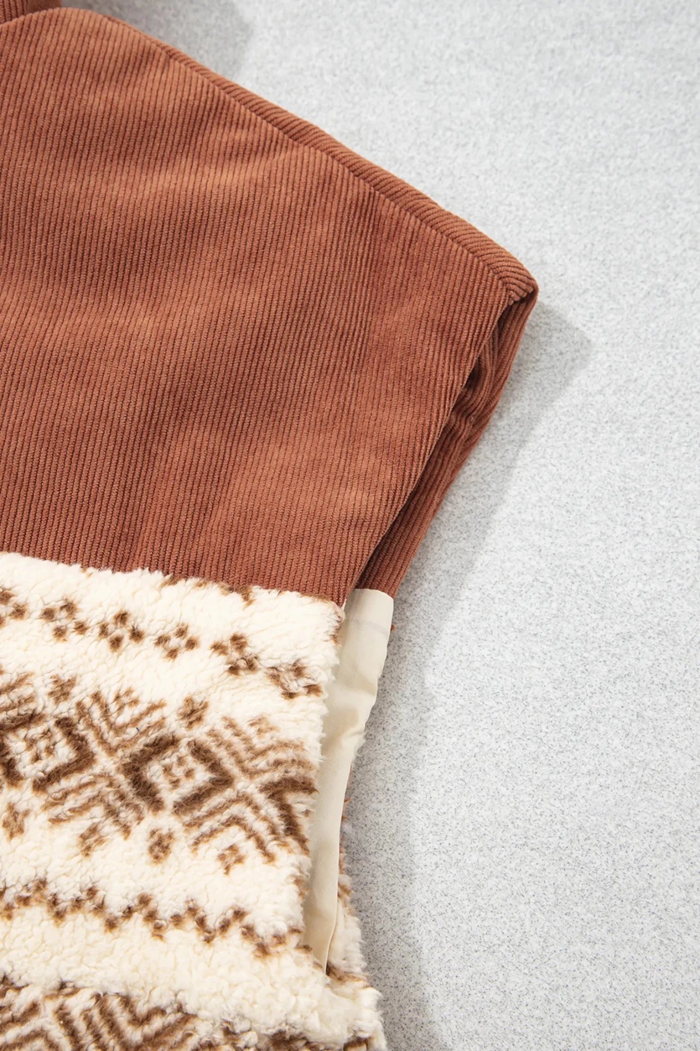 Folded brown corduroy garment with cream sherpa lining and brown geometric pattern.