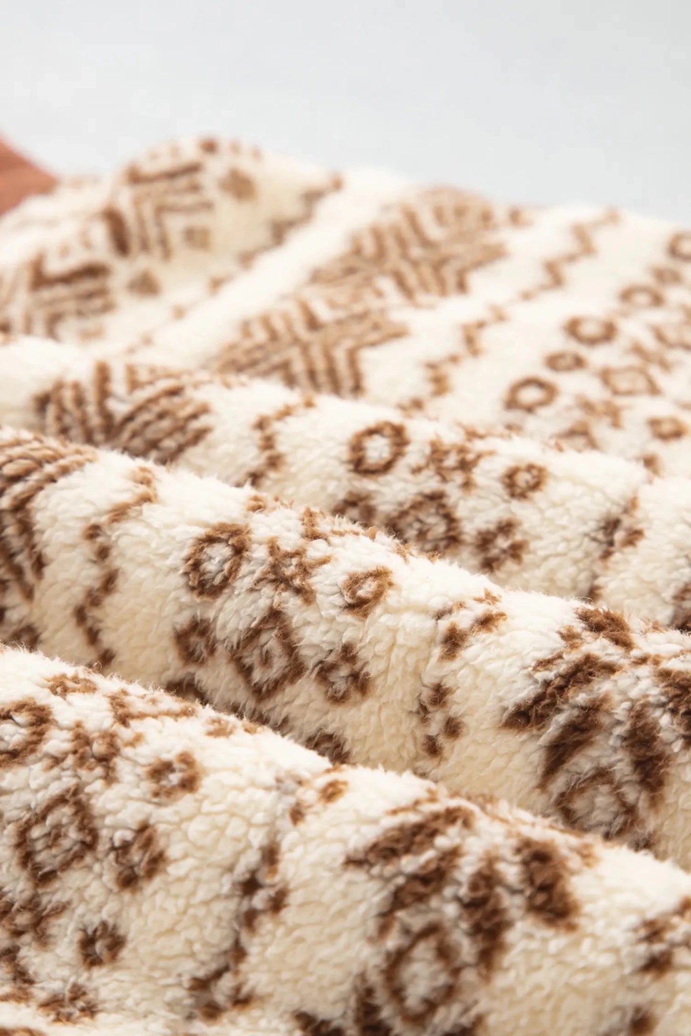 Close-up of a plush fleece blanket with a brown geometric pattern on a cream background.