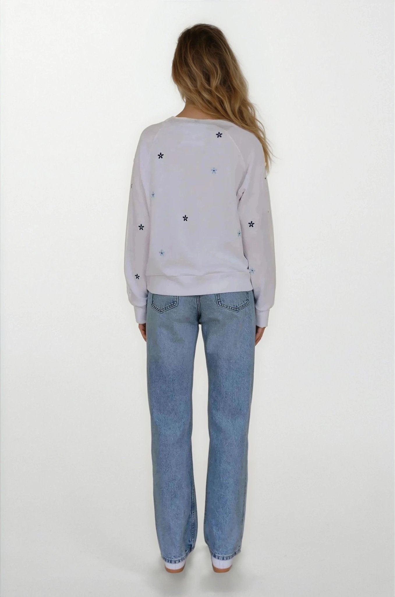 Person wearing a light gray sweatshirt with star patterns and blue jeans on a white background