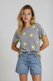Woman wearing a gray t-shirt with green star patterns and denim shorts on a plain background