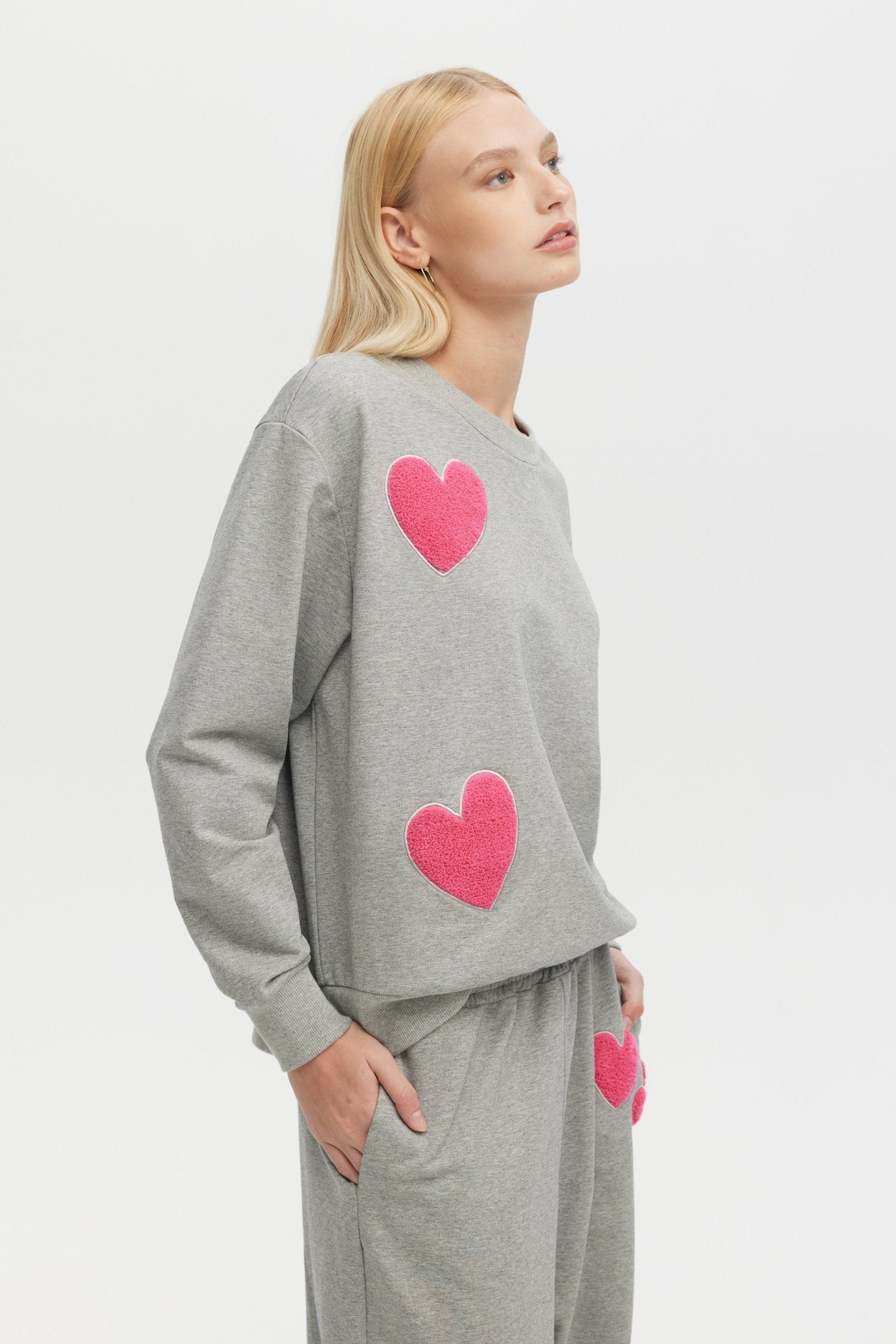 Woman wearing a gray sweatshirt with pink hearts on a white background