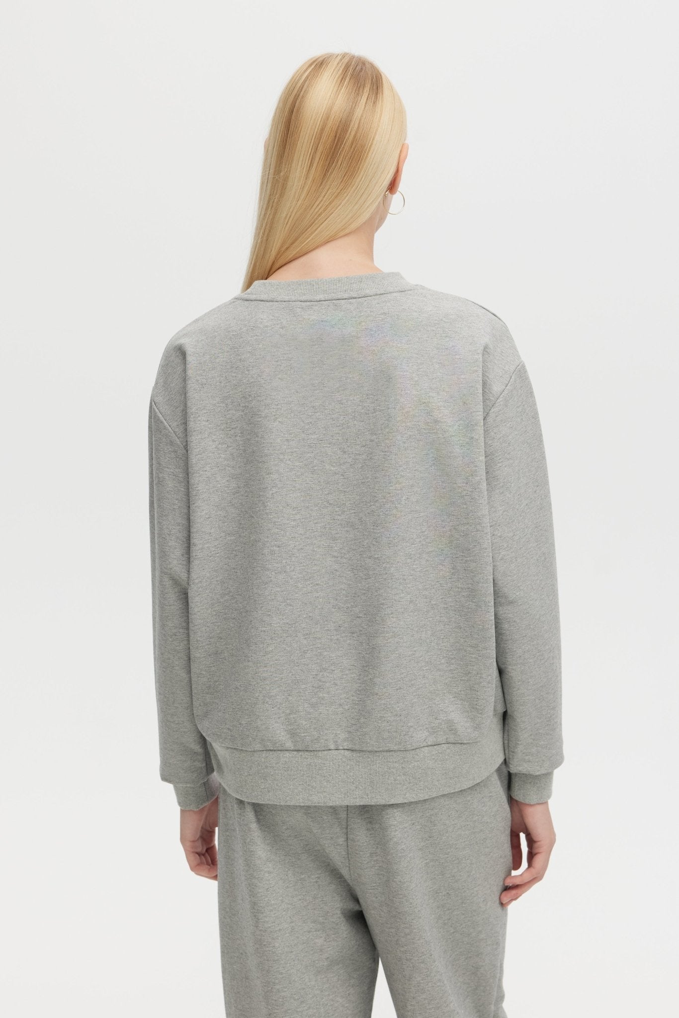Person wearing a gray sweatshirt and pants on a white background