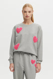 Person wearing a gray sweater with pink heart patterns on a light gray background