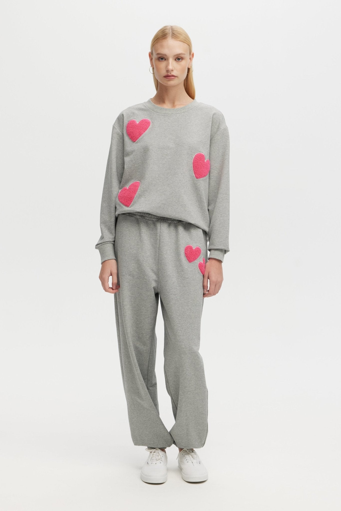 Person wearing a gray outfit with pink heart patterns on a white background