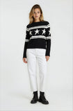 Woman wearing a black sweater with star patterns and white pants on a white background