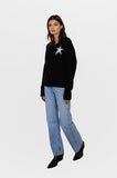Woman wearing a black sweater with a star design and light blue jeans on a white background