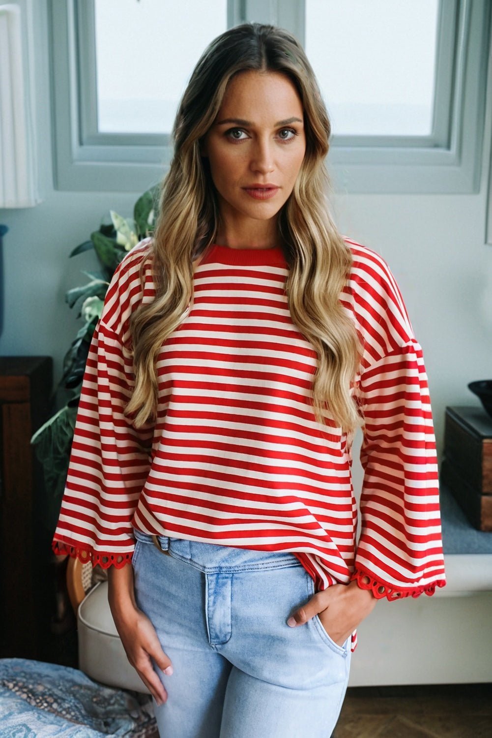 Woman wearing a red and white striped sweater and light blue jeans indoors.