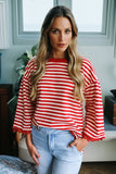 Woman wearing a red and white striped sweater and light blue jeans indoors.