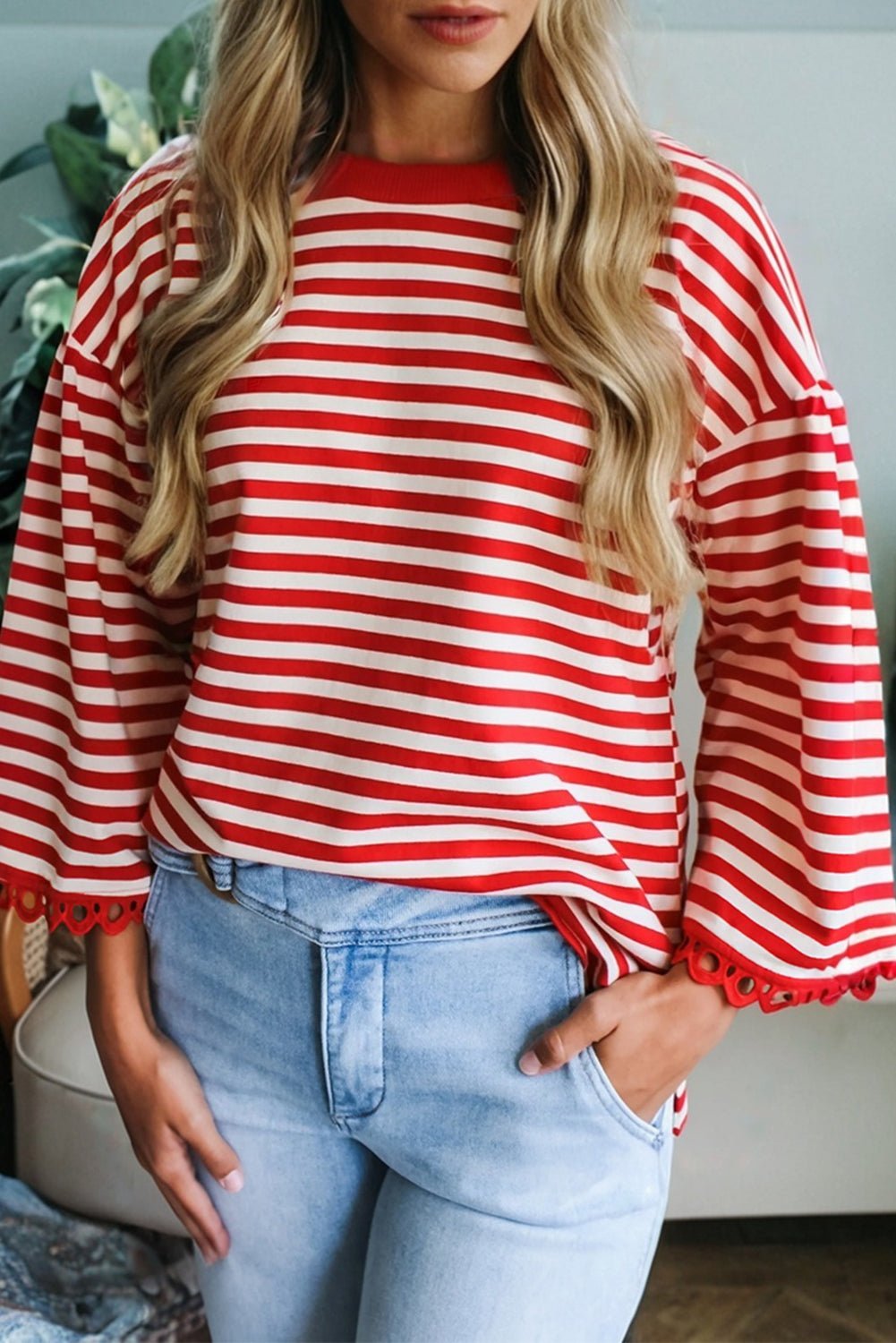 Person wearing a red and white striped sweater with bell sleeves and light blue jeans.