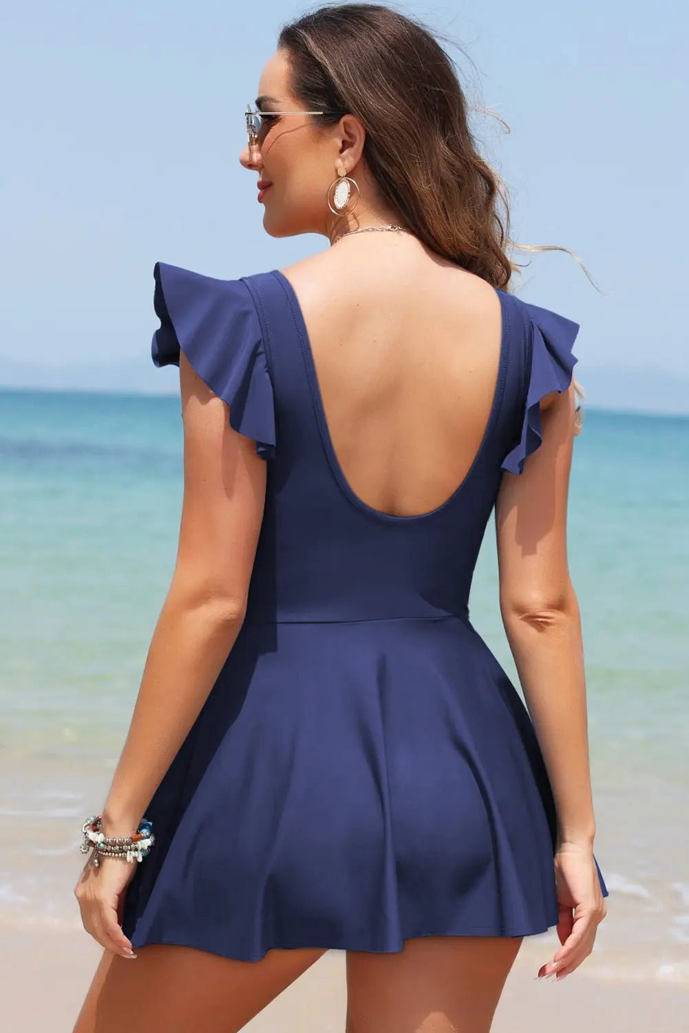 Woman in a navy blue dress with ruffled sleeves standing on a beach.
