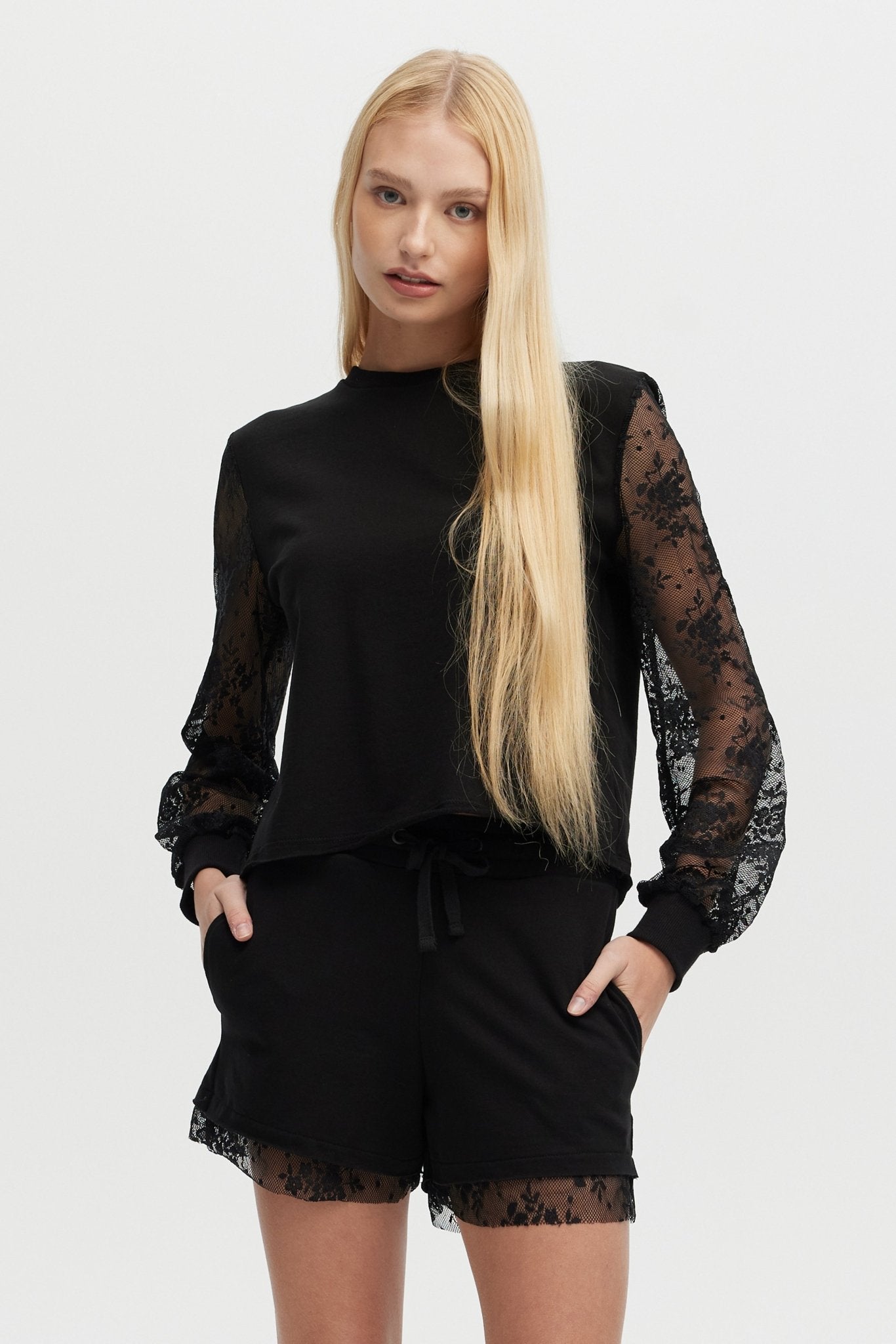 Woman wearing a black outfit with lace sleeves and shorts on a white background