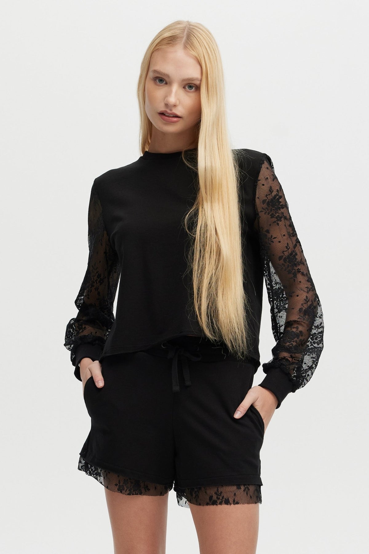 Woman wearing a black outfit with lace sleeves and shorts on a white background
