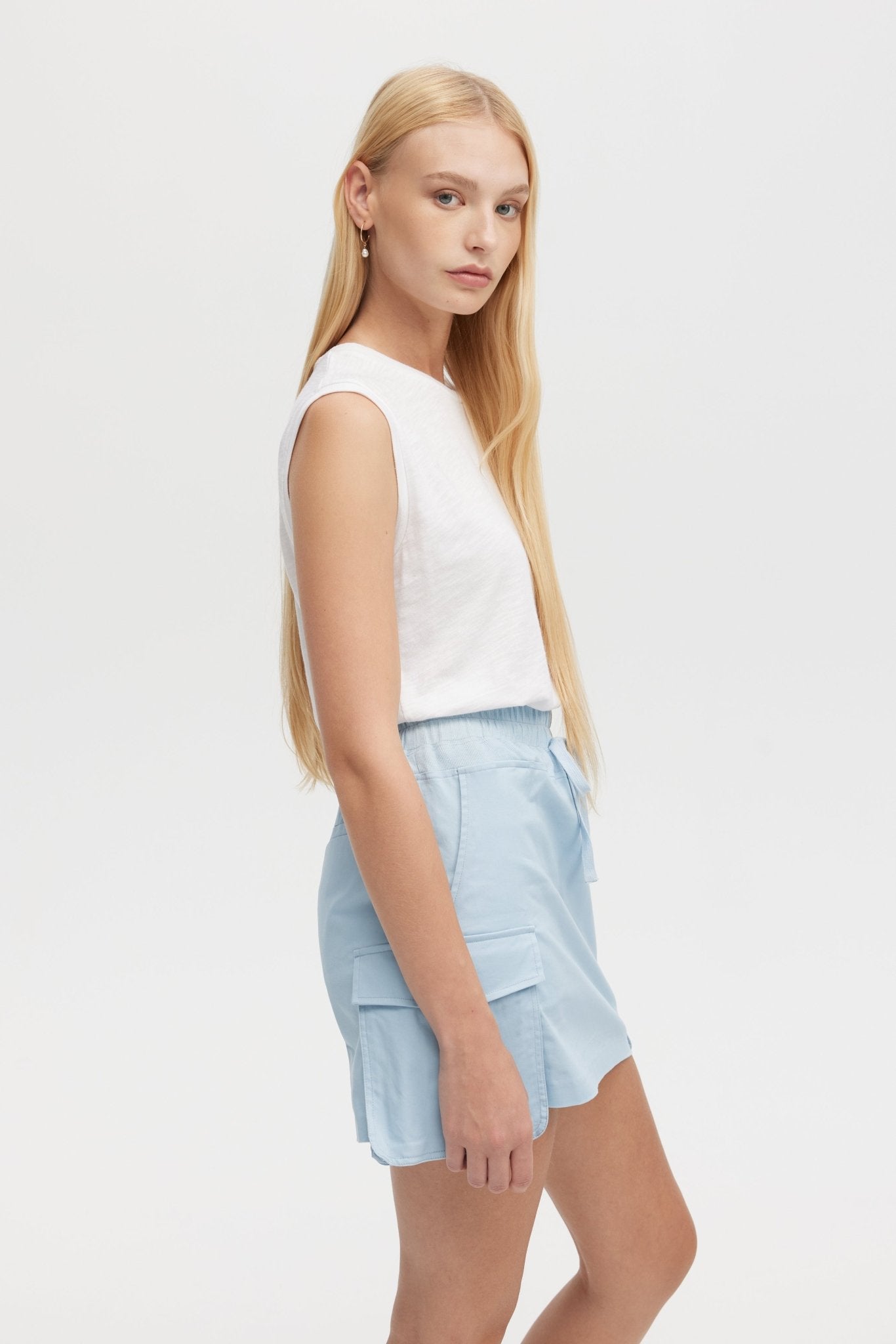 Woman wearing a white sleeveless top and light blue shorts on a white background