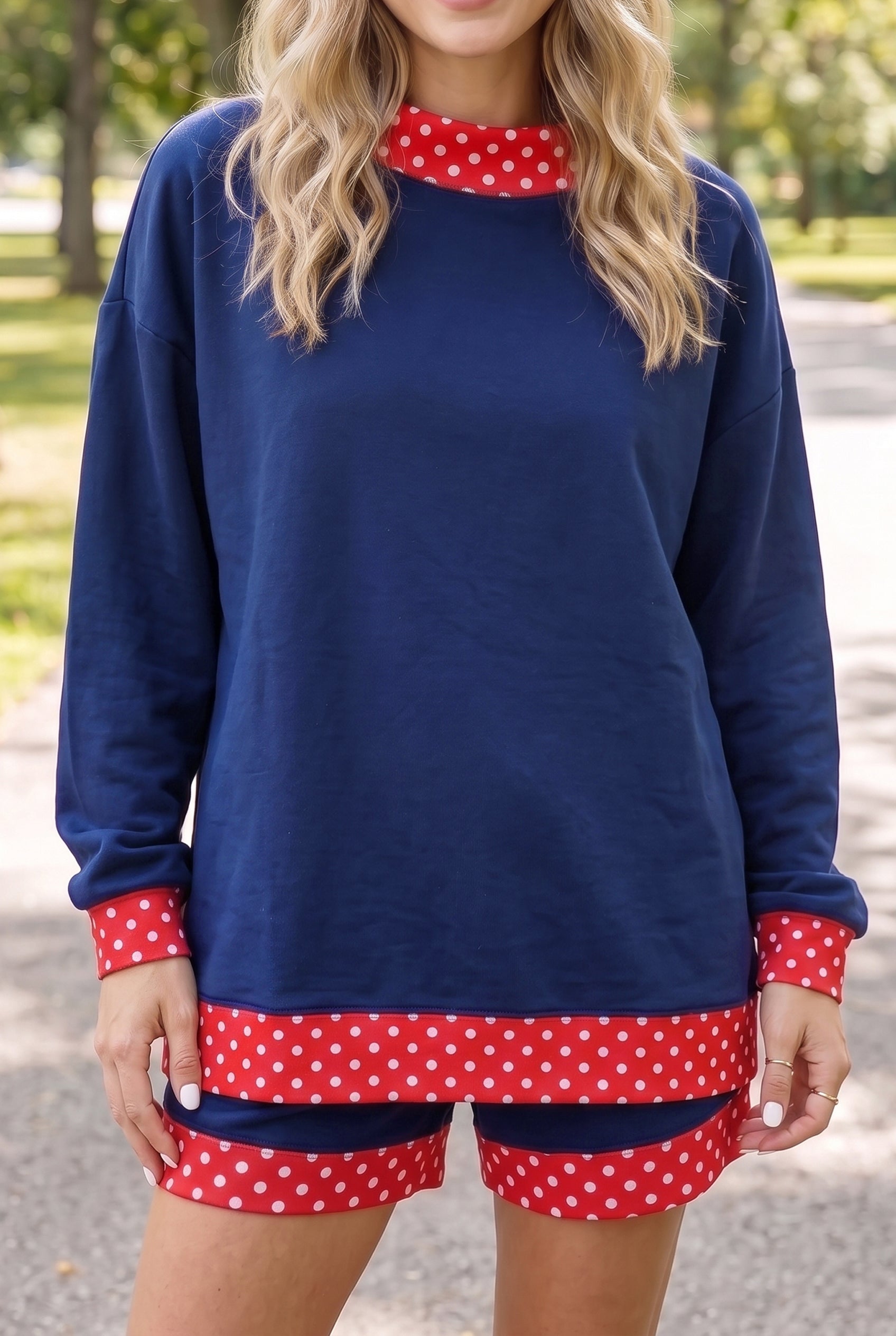 Woman wearing navy blue lounge set with red-white polka-dot trim, photographed outdoors on a blurred park path.