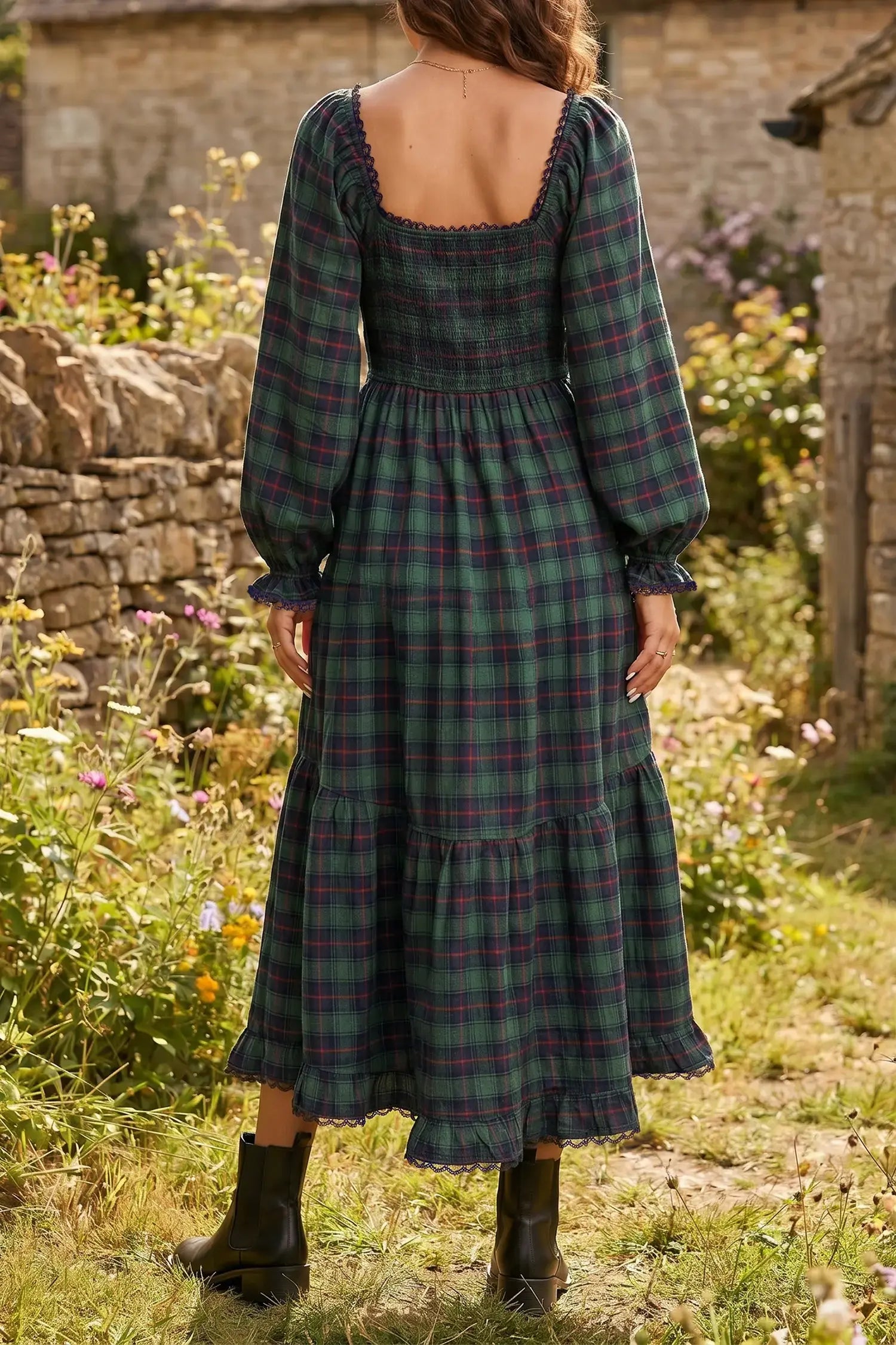 A woman wearing a long-sleeve plaid midi dress with a smocked bodice and tiered skirt, photographed from the back in an outdoor garden setting.