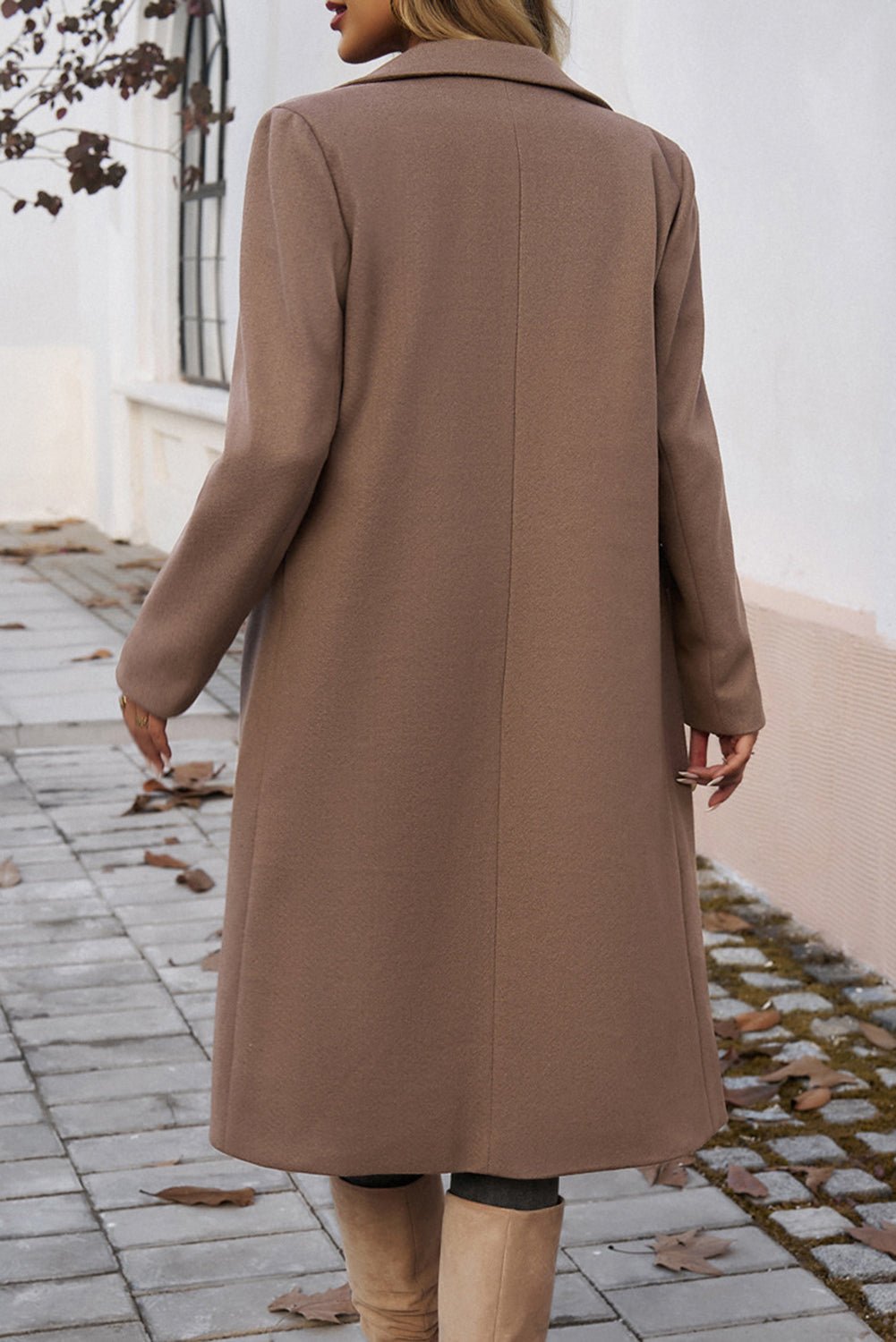 Person wearing a long brown coat walking on a paved path.