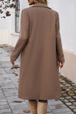 Person wearing a long brown coat walking on a paved path.