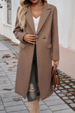 Person wearing a long brown coat holding a brown handbag on a sidewalk.