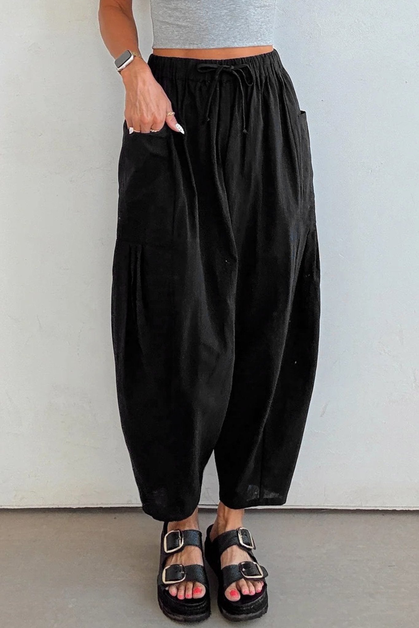 Person wearing black wide-leg pants and black sandals against a white background