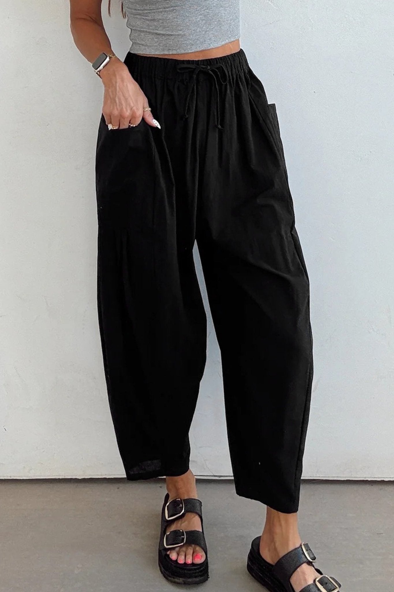 Person wearing black wide-leg pants and a gray top against a white wall.