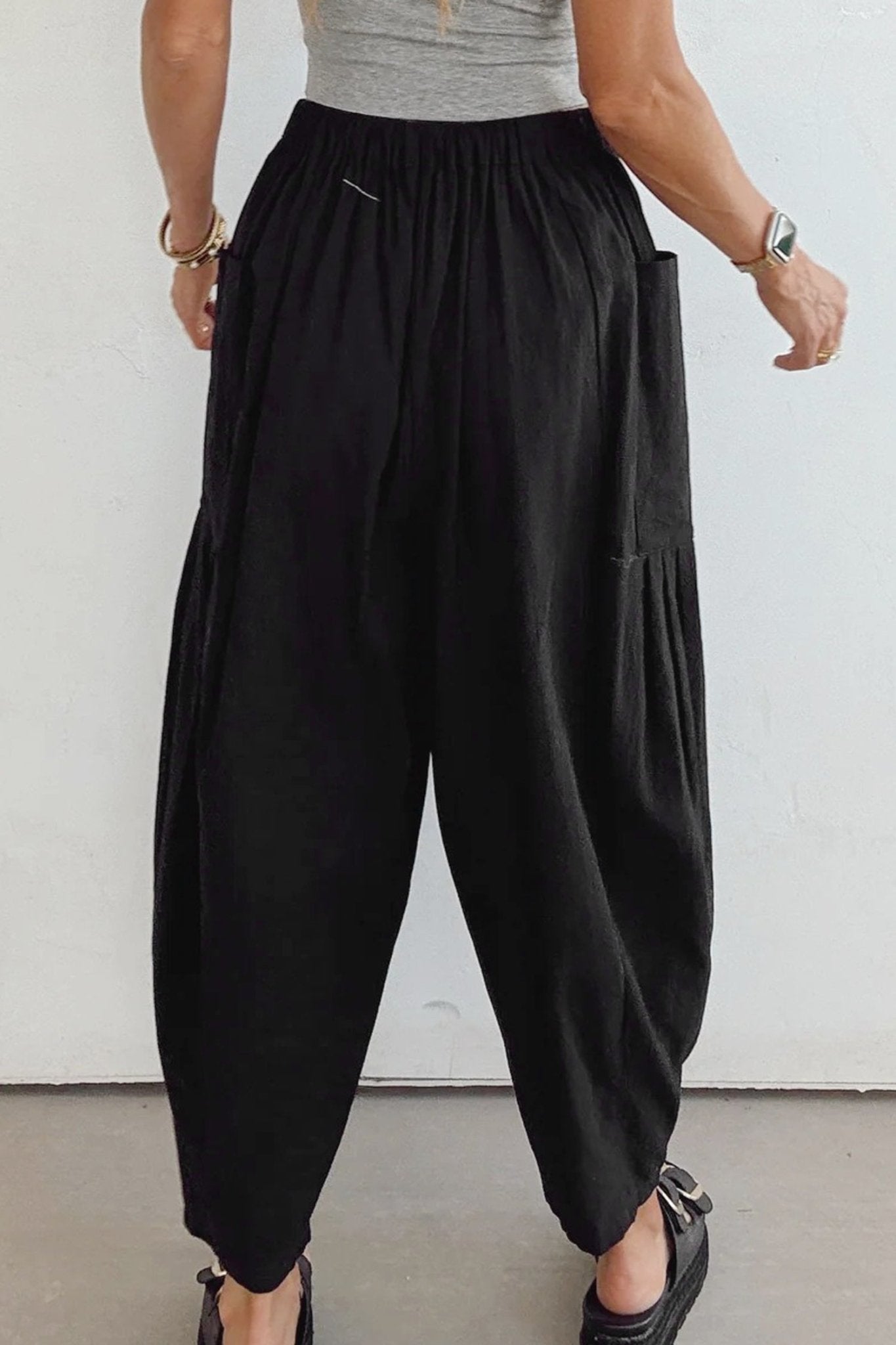 Person wearing black wide-leg pants and a gray top against a white background