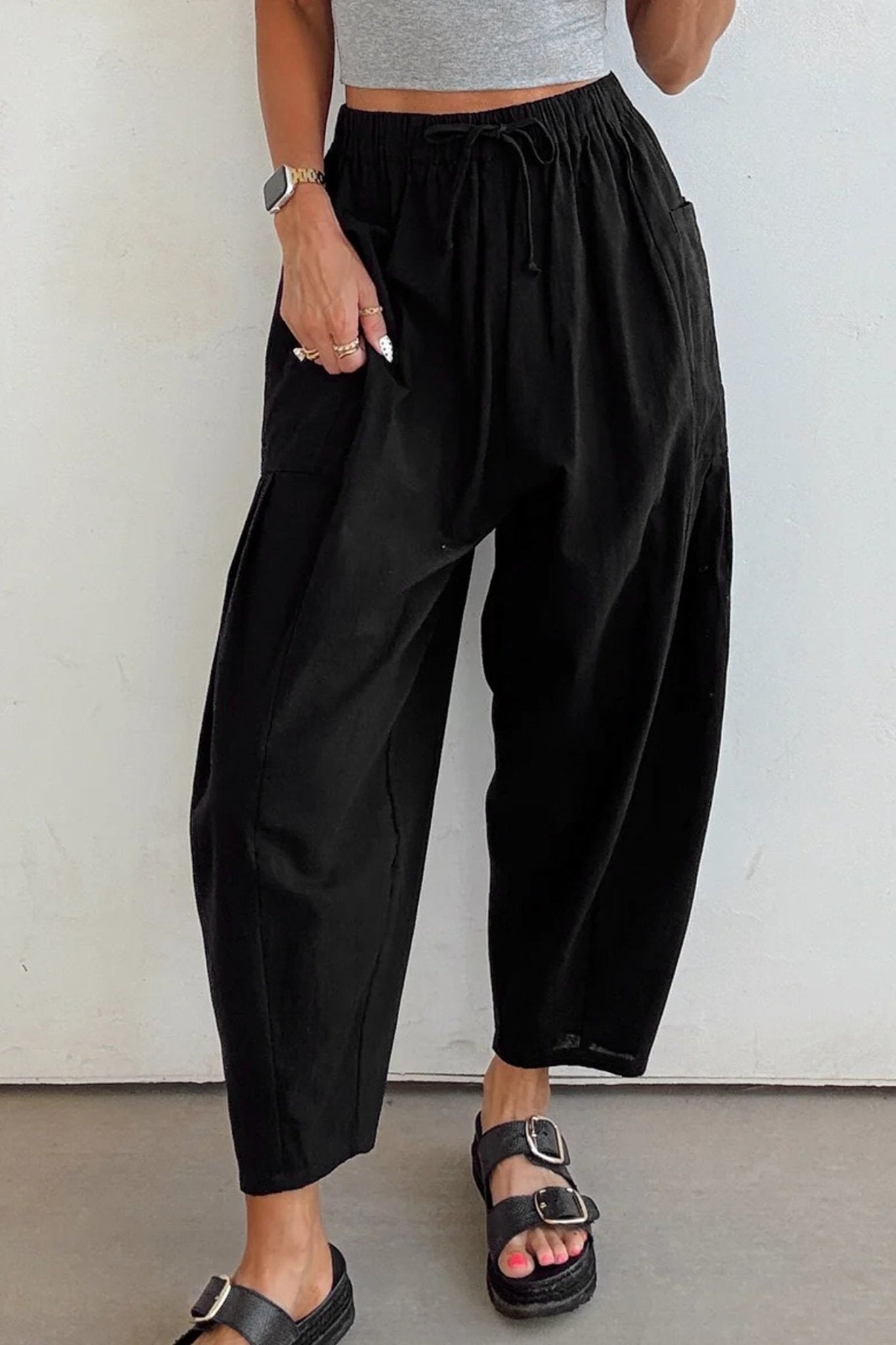 Person wearing black wide-leg pants and a gray top against a white background