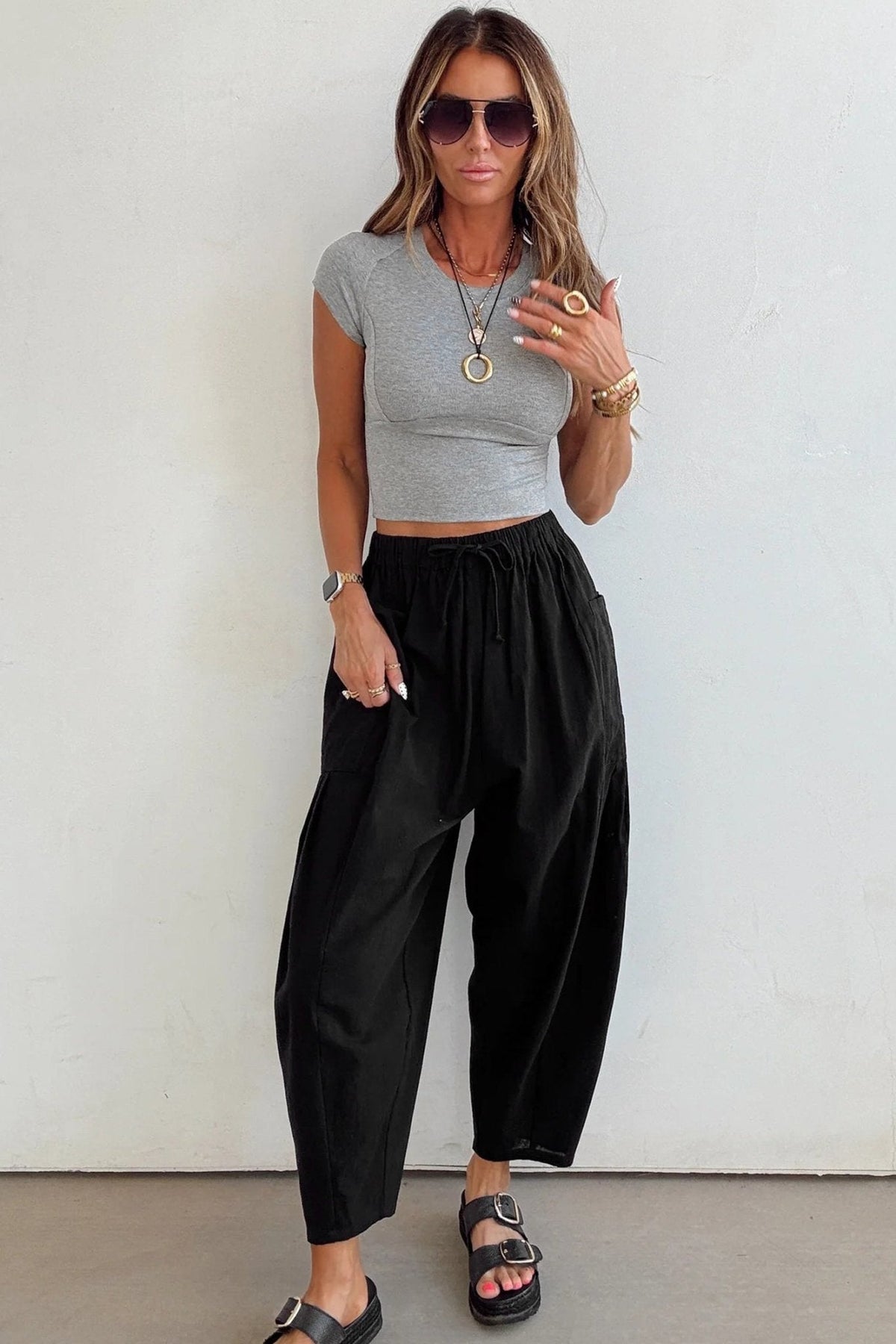 Woman wearing a gray crop top and black high-waisted pants against a white background