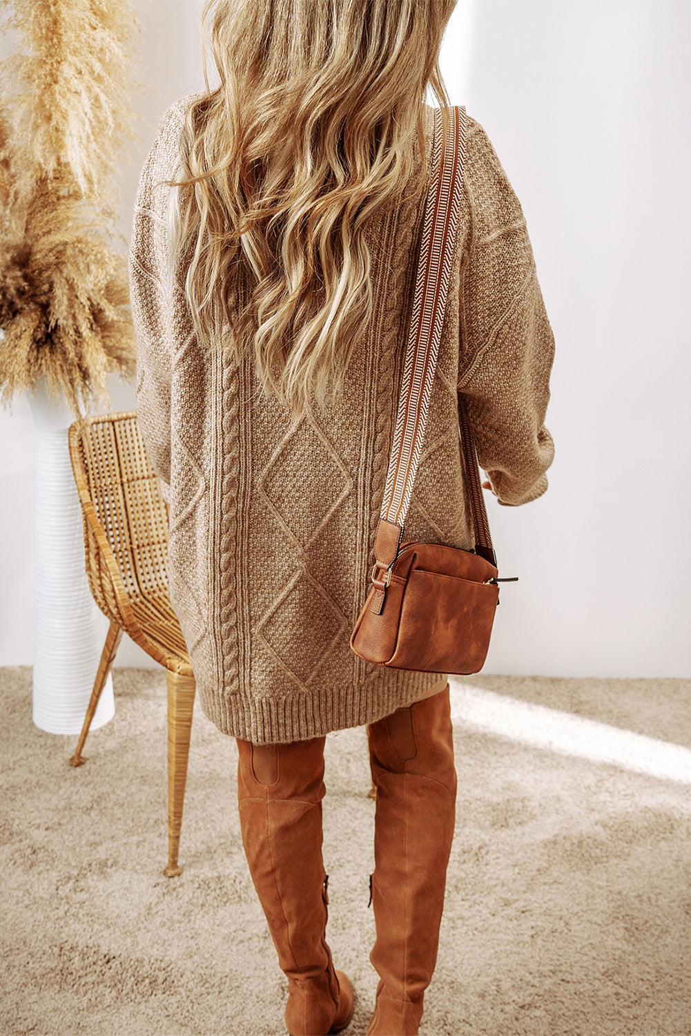 Person wearing a brown knitted cardigan and brown boots, holding a brown handbag indoors.