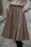 Person wearing a brown-beige herringbone skirt with pockets and gray sweater.