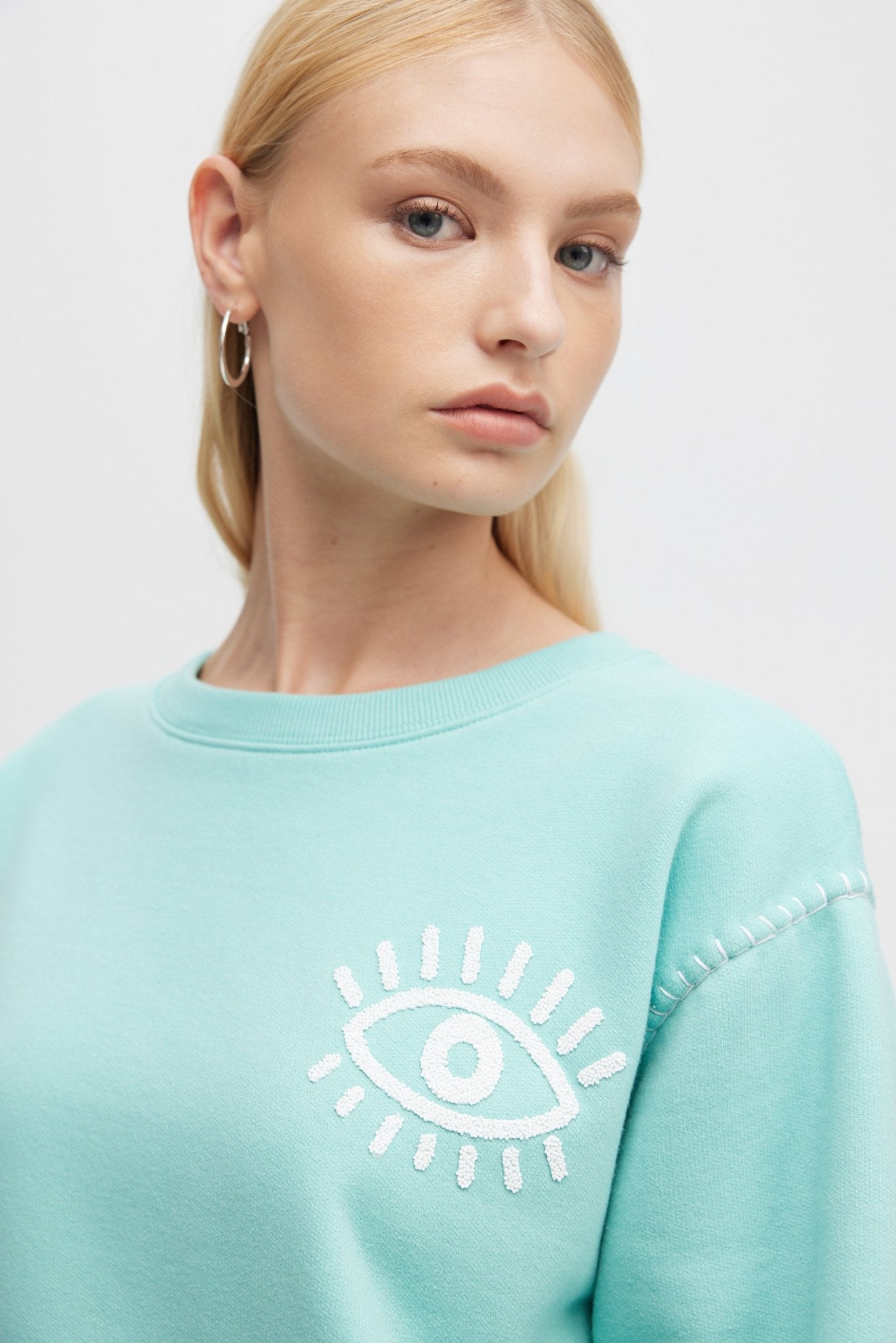 Person wearing a light blue sweatshirt with a white eye design on a plain background