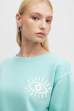 Person wearing a light blue sweatshirt with a white eye design on a plain background