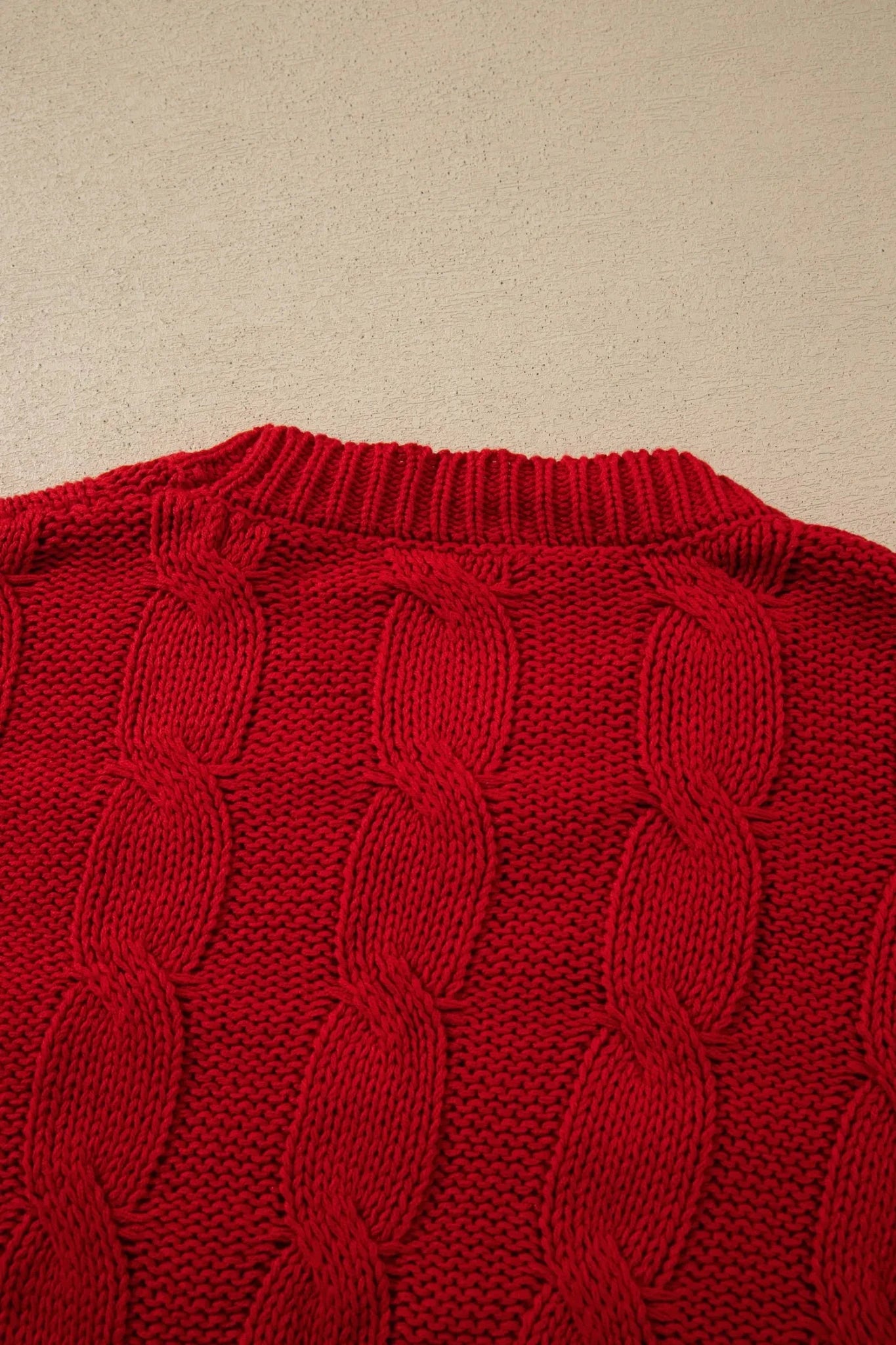 Close-up of red cable-knit sweater with ribbed crew neck and textured
