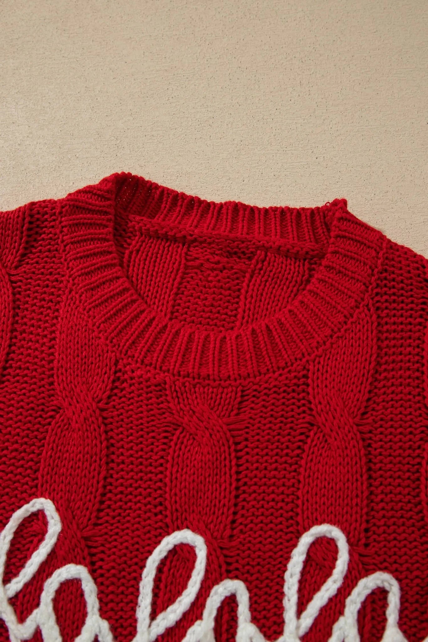 Close-up of red cable-knit sweater with white cursive script graphic.