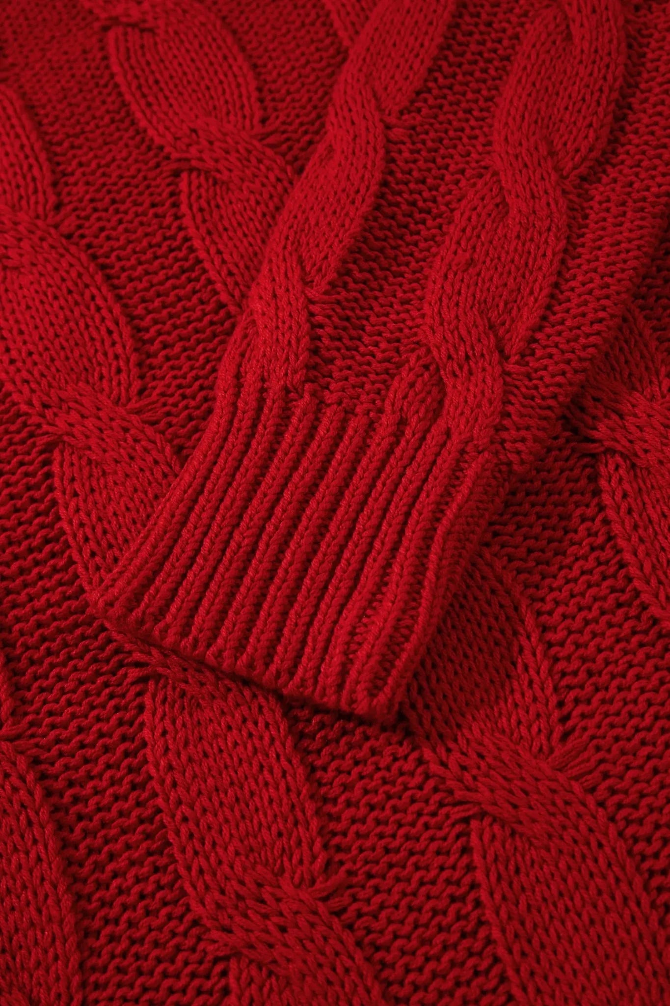 A close-up of a vibrant red cable-knit sweater, highlighting the detailed knit pattern and ribbed cuff.
