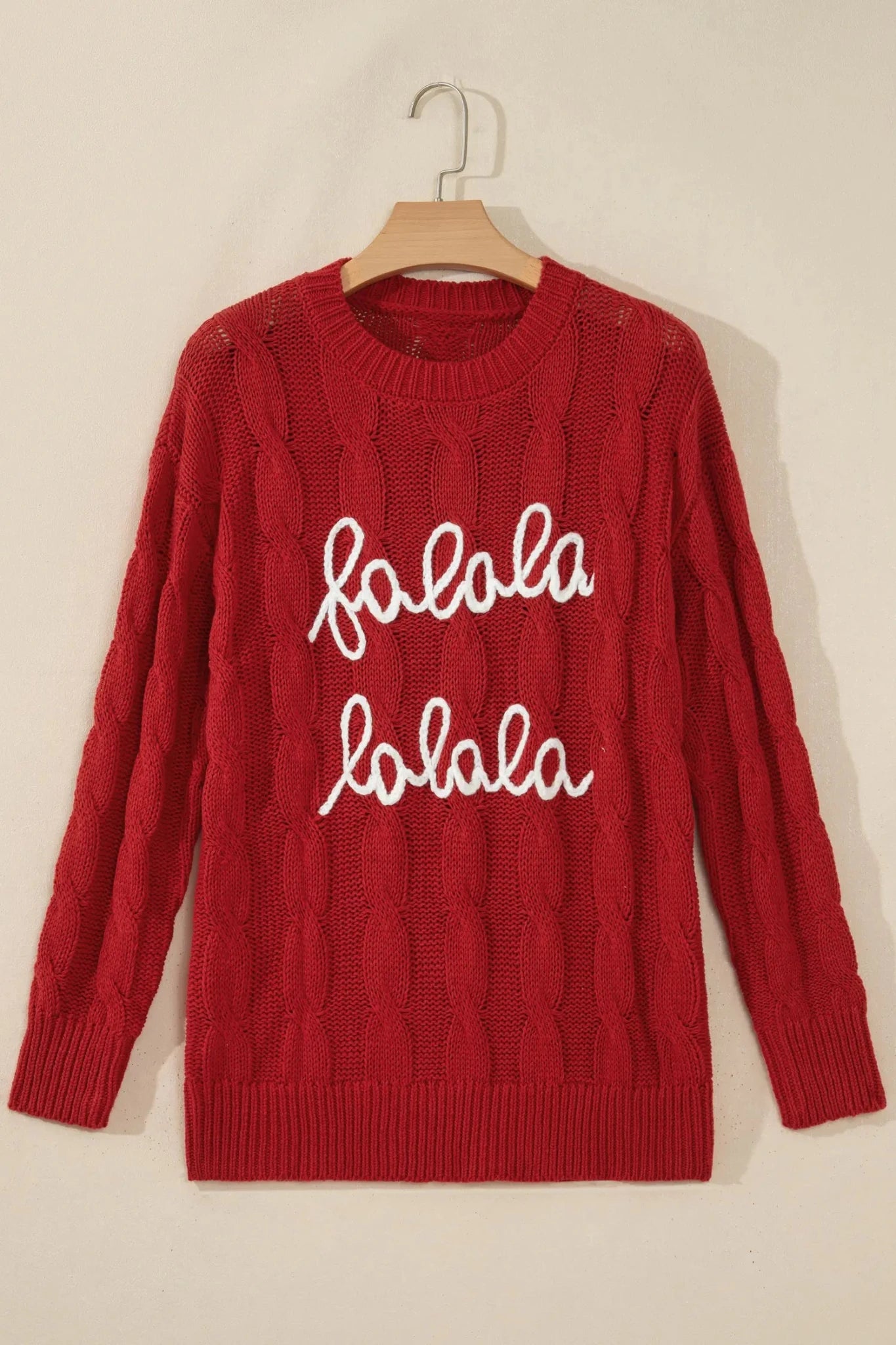 Red cable-knit “folala folala” sweater with white script on wooden hanger.