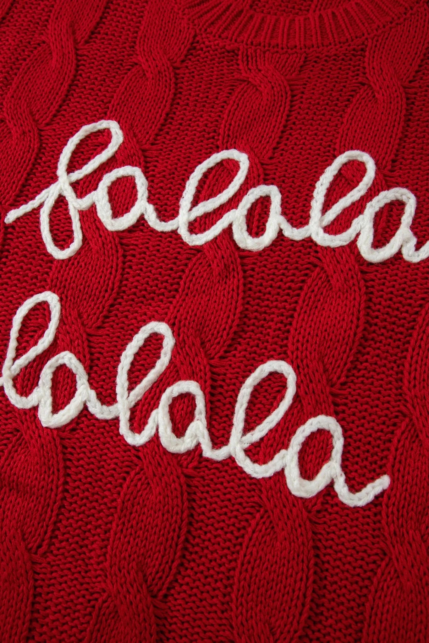 Close-up of red cable-knit sweater with repeated white “lala” script.