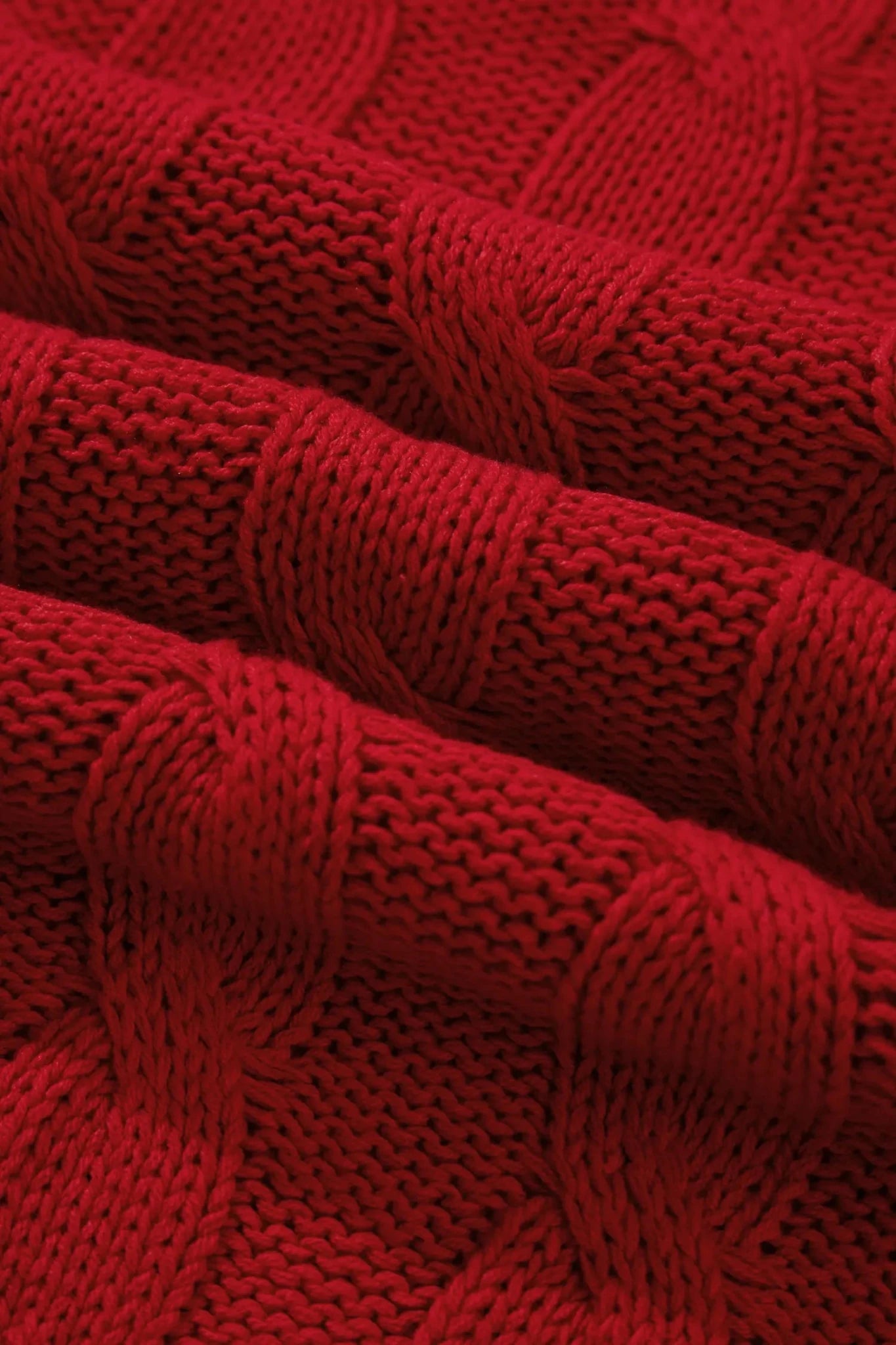 A close-up of a red cable-knit fabric with a textured, ribbed pattern and soft folds.