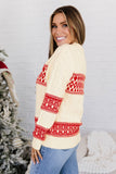 Woman in cream cable-knit Fair Isle sweater with red patterns and blue jeans.