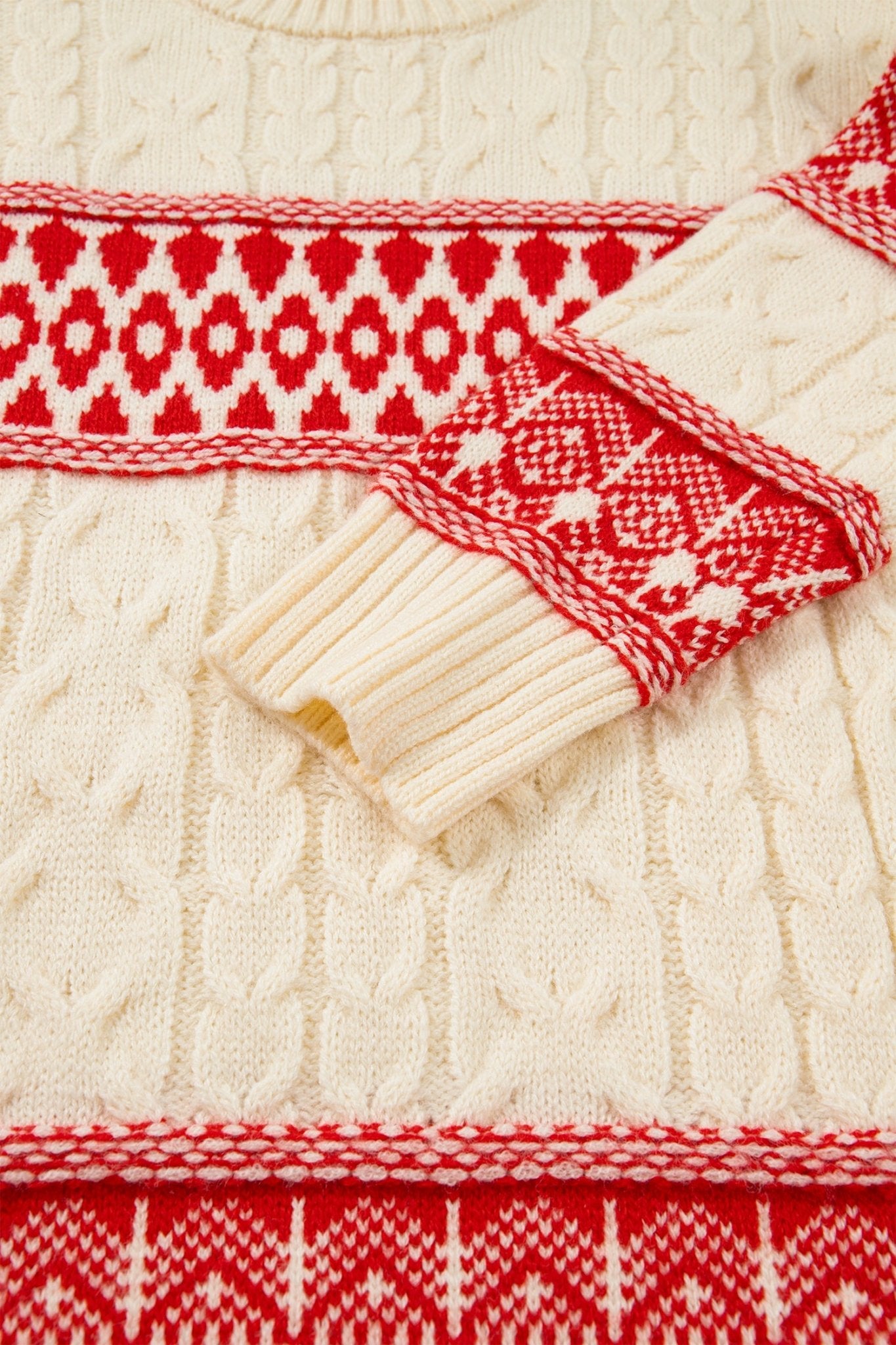 Close-up of a cream cable-knit sweater with red and white Fair Isle patterned trim and cuffs.